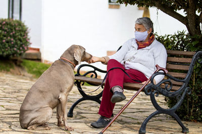 Full length of senior wearing mask with dog sitting outdoors