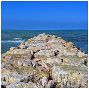 Rocks on beach by sea against blue sky