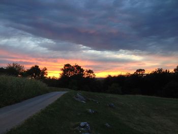 Road passing through field against cloudy sky