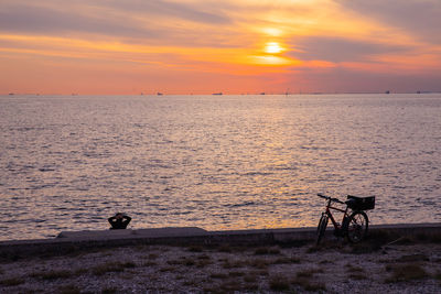 Silhouette bicycle on beach against sky during sunset