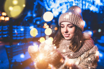 Portrait of smiling young woman in illuminated park during winter