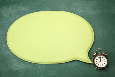 High angle view of blank green speech bubble with alarm clock on blackboard