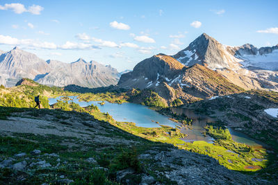 Silhouetted hiker walks down ridge towards limestone lakes in rockies