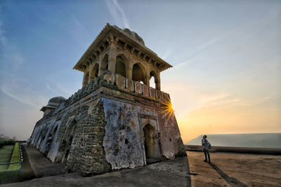 Young man standing by historic building against sky during sunset