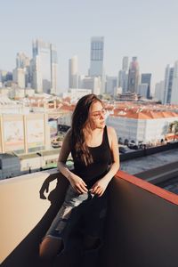 Young woman wearing sunglasses standing against building in terrace