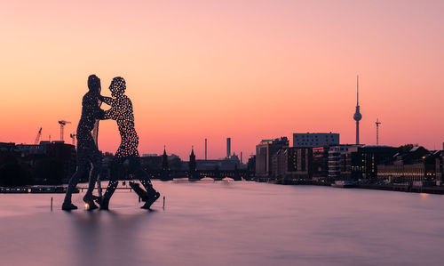 View of sculpture and buildings against sky during sunset