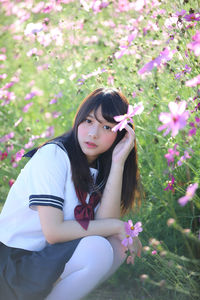 Portrait of student wearing school uniform while crouching by flowering plants on land during sunny day