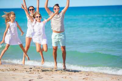 Cheerful family jumping on beach with arms raised