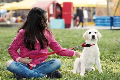 Girl with dog sitting on grassy field at park