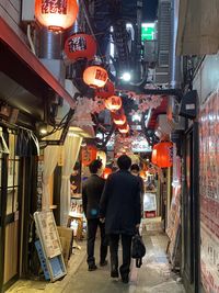 Rear view of people walking on illuminated street at night