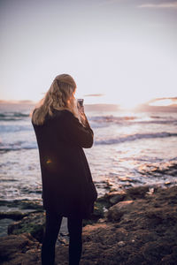 Rear view of woman standing at beach against clear sky