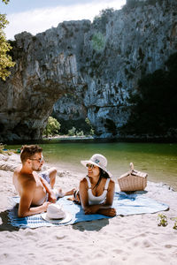 Full length of couple relaxing on beach against rock formation