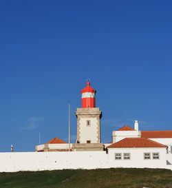 Low angle view of lighthouse by building against clear blue sky