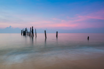 Wooden posts in sea against sky during sunset