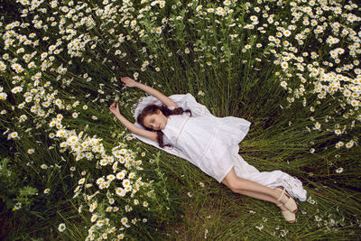 Girl child lies on a camomile field in a white dress in summer