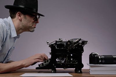 Side view of mature man using typewriter on table against wall at office