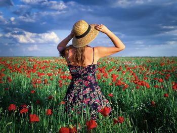 Rear view of woman standing by poppy field against sky