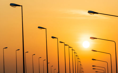 Low angle view of street lights against orange sky