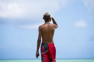 Rear view of shirtless man standing in sea against sky