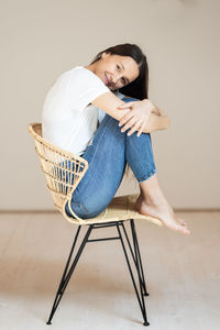 Portrait of young woman sitting on chair against wall