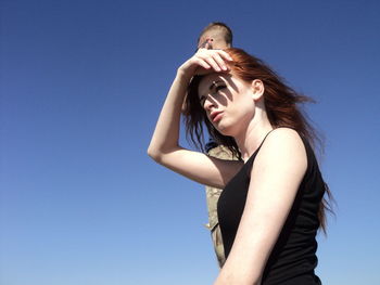 Young woman shielding eyes against clear blue sky