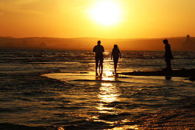 Silhouette people on beach against sky during sunset