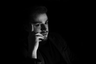 Close-up of handsome man with hand on chin against black background