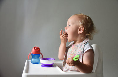 Almost 2 years old baby girl eating rice porridge with her hand. grey background.