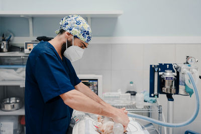 Focused male veterinarian in uniform and respiratory mask using medical instruments during surgery in hospital