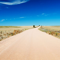 Road amidst land against blue sky