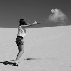 Woman throwing sand at beach against sky