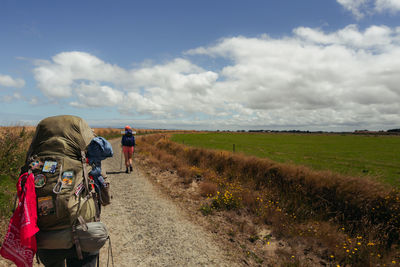 Rear view of people with backpacks walking on dirt road