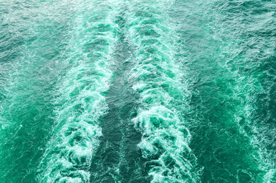 Stormy foam and a ship's track on the turquoise sea water.