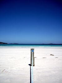 Wooden posts on beach against clear blue sky