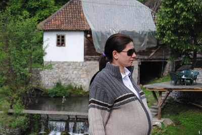 Pregnant woman wearing sunglasses and jacket standing against house