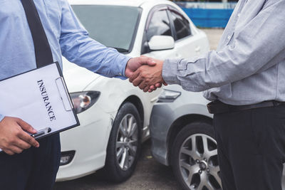 Midsection of man shaking hand with insurance agent by cars