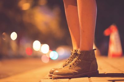 Low section of woman standing on footpath at night