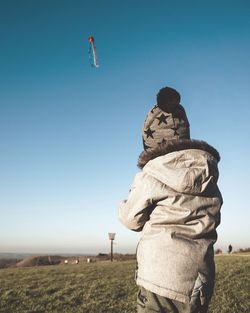 Rear view of boy wearing warm clothing while flying kite against clear sky