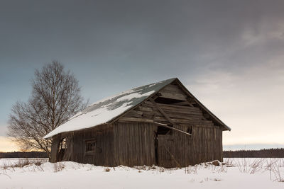 Abandoned house on snow covered field against cloudy sky