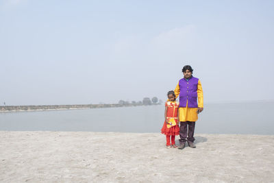 Full length portrait of father with daughter standing against sea and sky