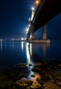 Illuminated bridge over river against sky at night