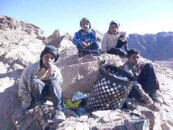 Friends sitting on rock formations amidst garbage can