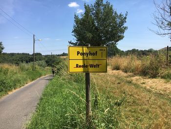 Information sign on road by trees against sky