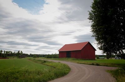 Road amidst field and houses against sky