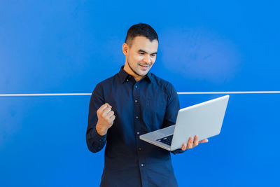 Man holding smart phone while standing against blue sky