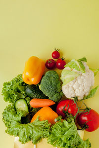 Tomatoes and vegetables on plate against yellow background