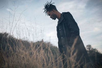 Side view of man standing on grassy field against sky