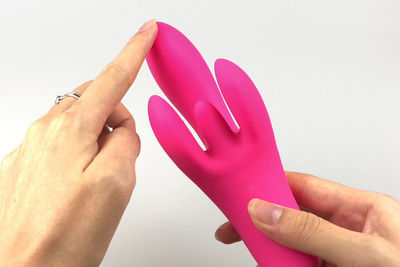 Close-up of hand holding pink flower against white background