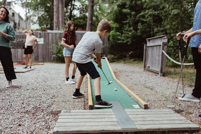 Family looking at boy taking shot while playing miniature golf in backyard