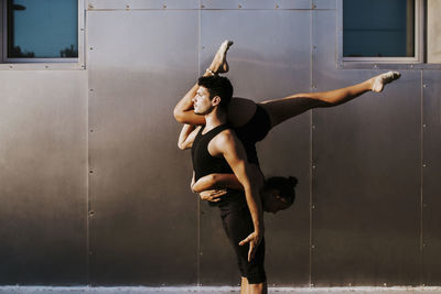 Professional male gymnast holding female upside down while doing dance posture by wall
